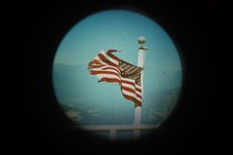 An illustration of a tattered American flag seen through the circle of a telescope.