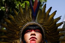 A close-up of a person looking up at the sky, wearing red paint in bold stripes on their face, and a feathered headdress
