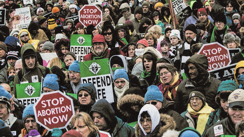 Picture of a march crowded with people holding signs that read"stop abortion now" and "defend life."