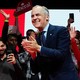 Mark Carney smiles and claps in front of a group of supporters waving, recording with their phones, and holding signs