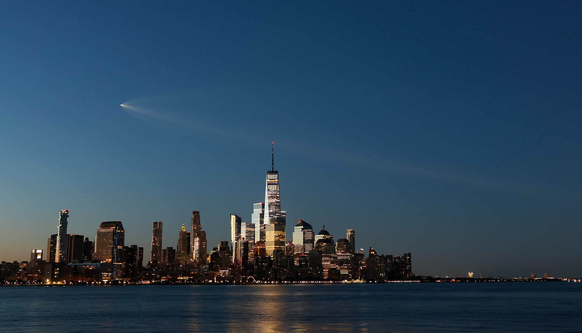 photo of New York City skyline at twilight with rocket streaking across sky leaving a trail