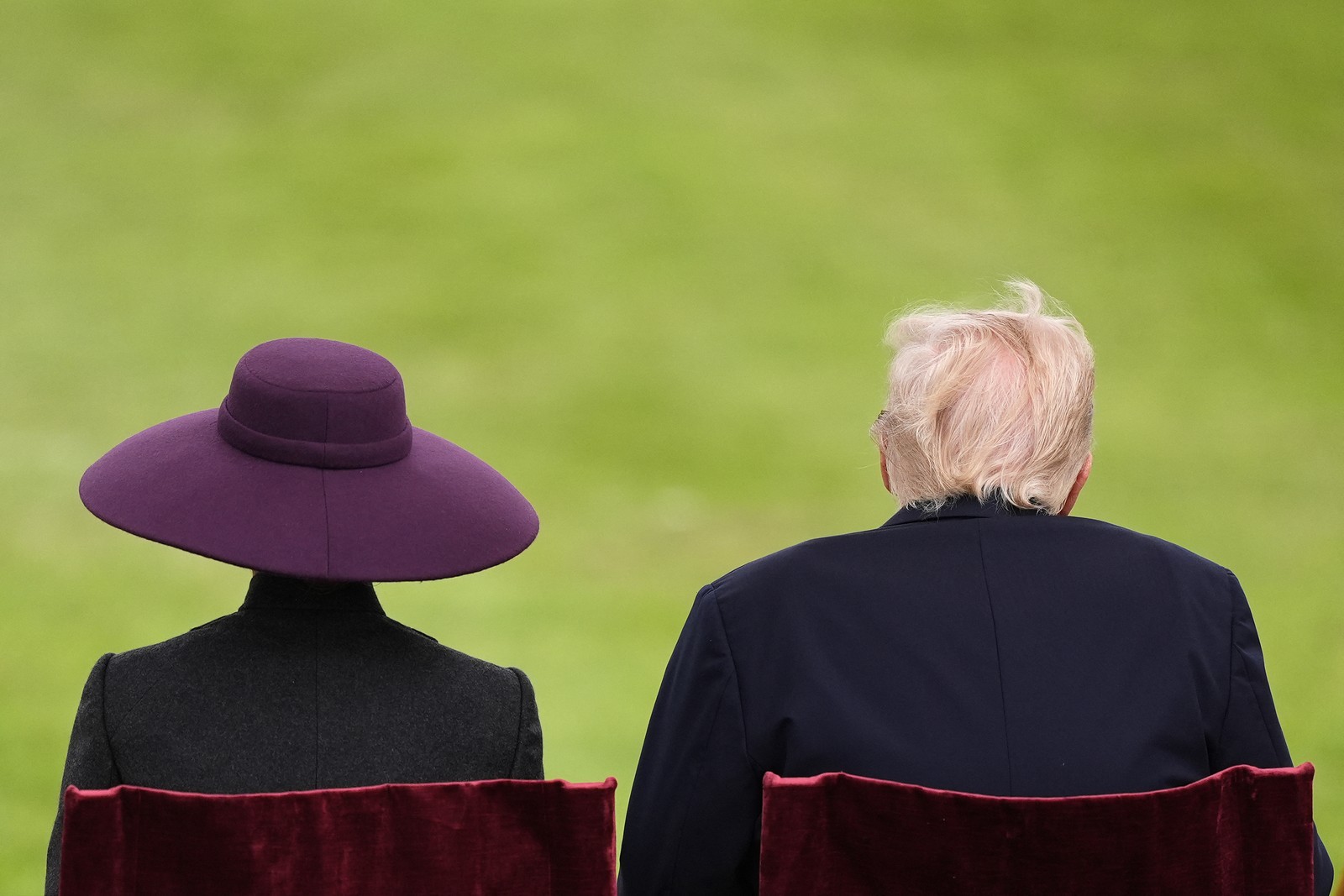 A view from behind of President Trump and his wife Melania, as they watch a military ceremony on a lawn of Windsor Castle. Melania is wearing a large purple hat.