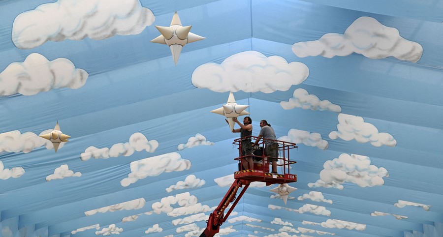 Workers stand on an elevated platform arranging ornaments inside a beer hall.