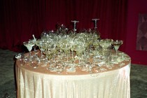 A table covered with a sparkling pink tablecloth is piled high with broken glassware and champagne flutes