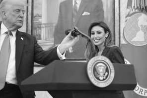 A black-and-white photo of Donald Trump touching a podium microphone while Alina Habba smiles in the background.