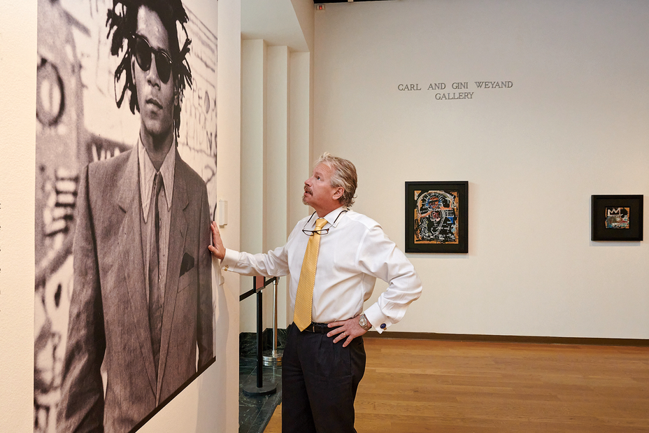 A man looking at a large portrait of Basquiat with two forged paintings hanging in the background.