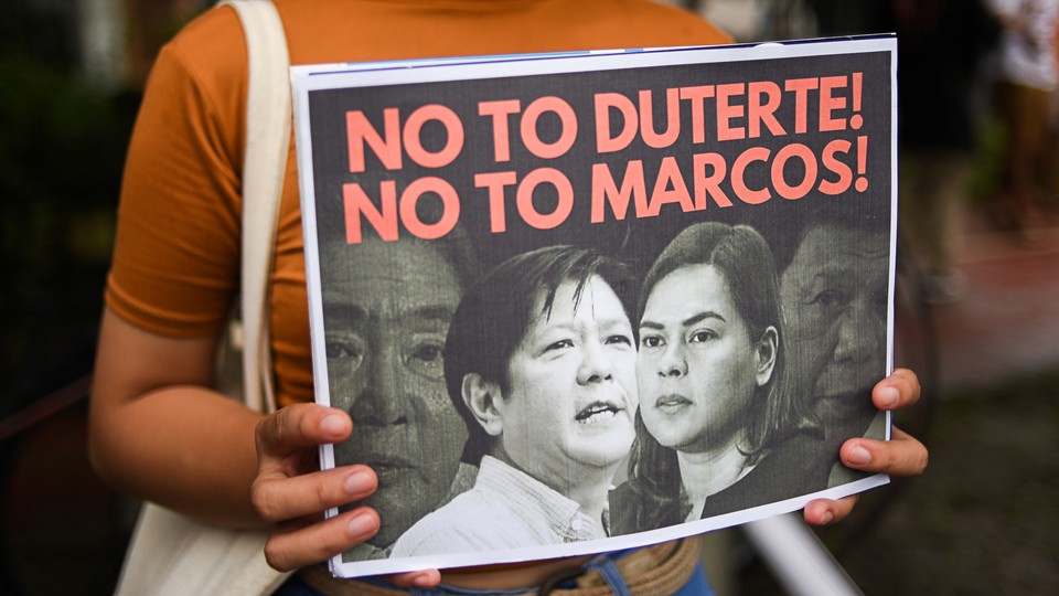 A person holding a sign reading "No to Duterte! No to Marcos!"