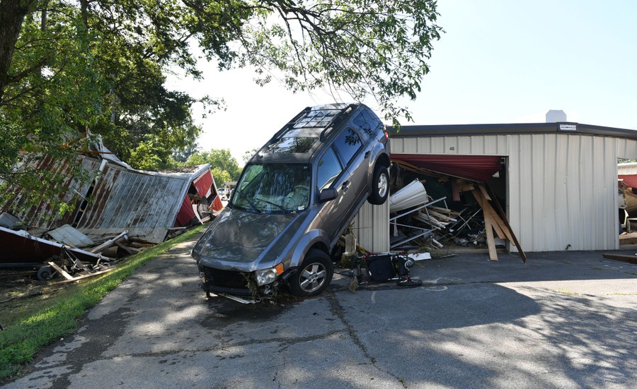 An SUV is seen upended, resting on a damaged building.