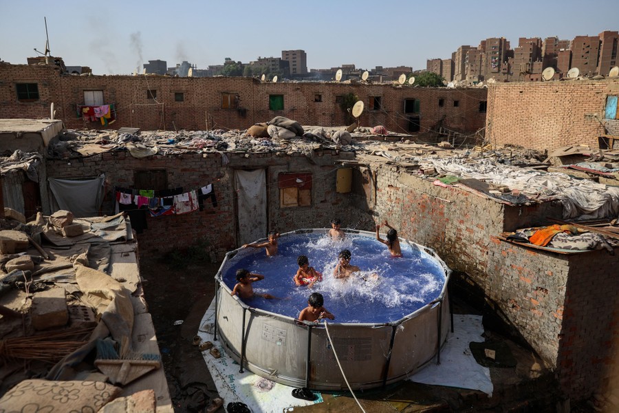 A half-dozen children splash in an above-ground swimming pool set up in a small courtyard.