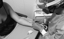a masked healthcare worker injects a monkeypox vaccine intradermally into a woman's arm. the needle is entering almost horizontal to the arm so it can be shallow.