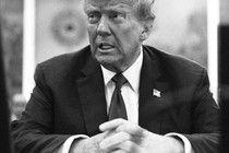 Black-and-white photo of Donald Trump in a suit siting with his hands crossed in front of him