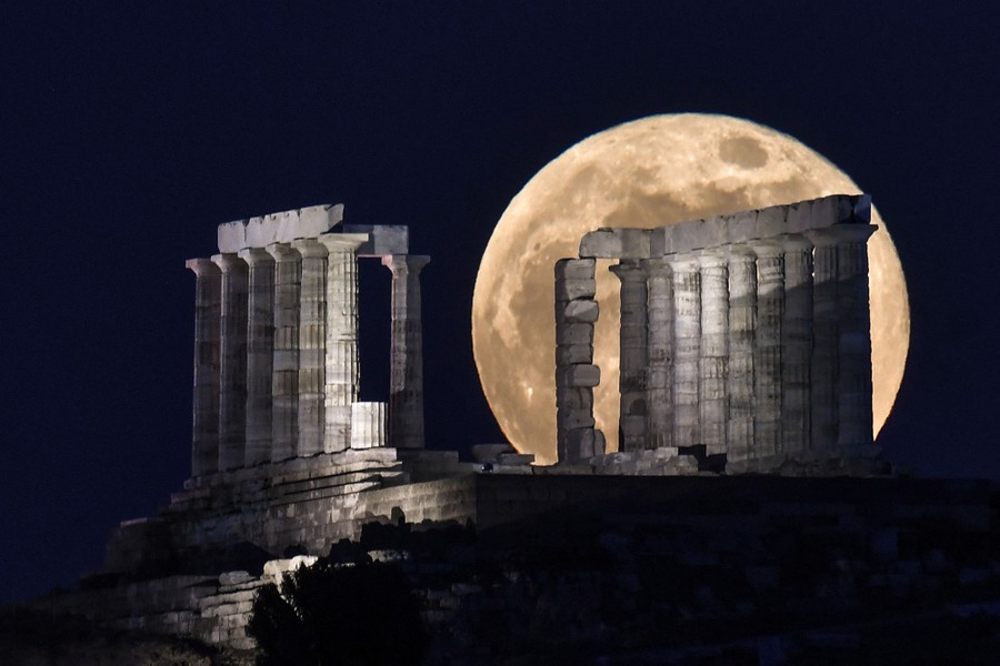 The moon rises behind an ancient Greek temple.