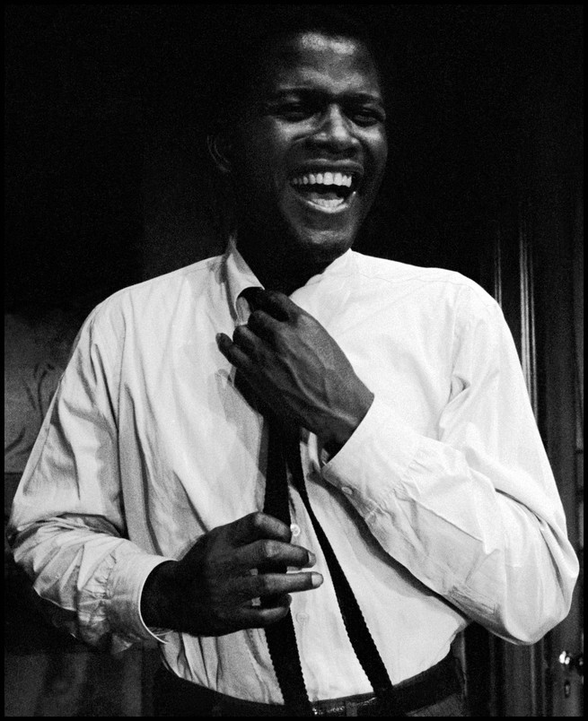 Poitier in a with hands to his tie laughing