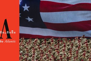 This photo shows a wide shot of U.S. army members saluting and wearing fatigues and matching red berets. Behind them is the image of the American flag