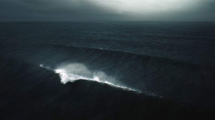 Una vista aérea de las olas que se extienden sobre un océano oscuro bajo un cielo nublado