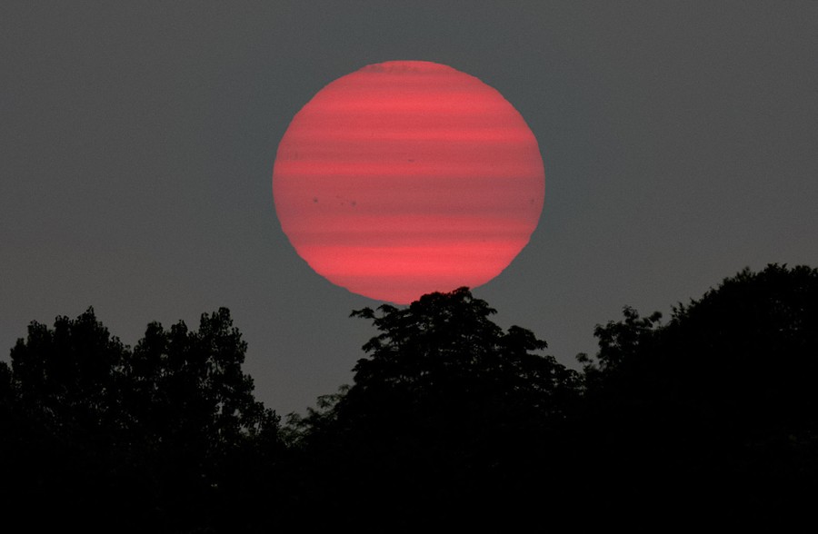 A magenta sun sets behind thin clouds, appearing striped.