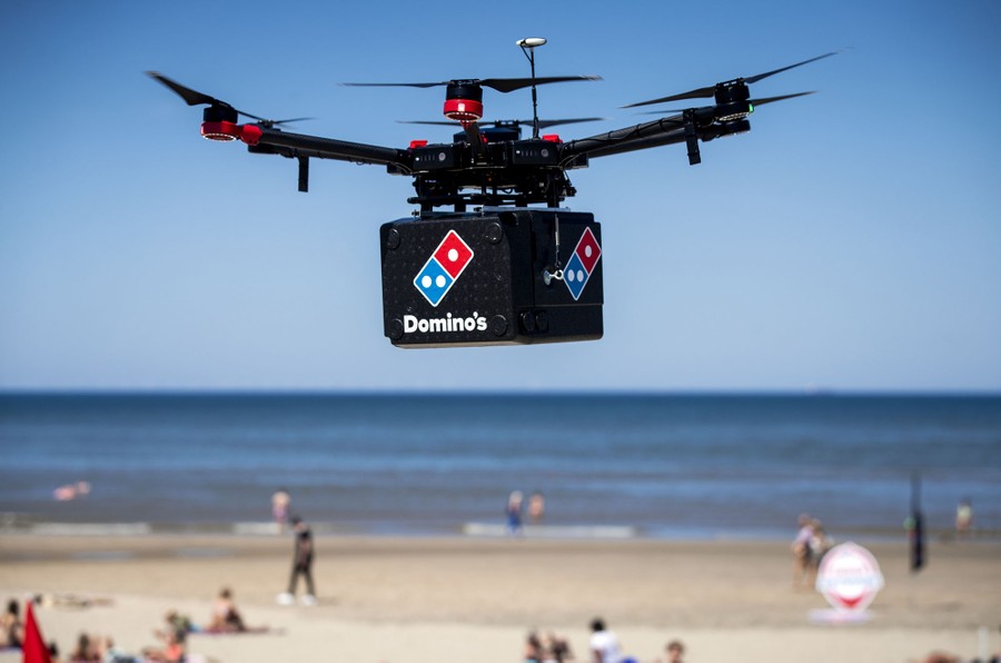 A robotic drone carries a box labeled as pizza.