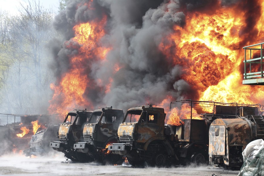 A huge fire burns among several parked military vehicles.