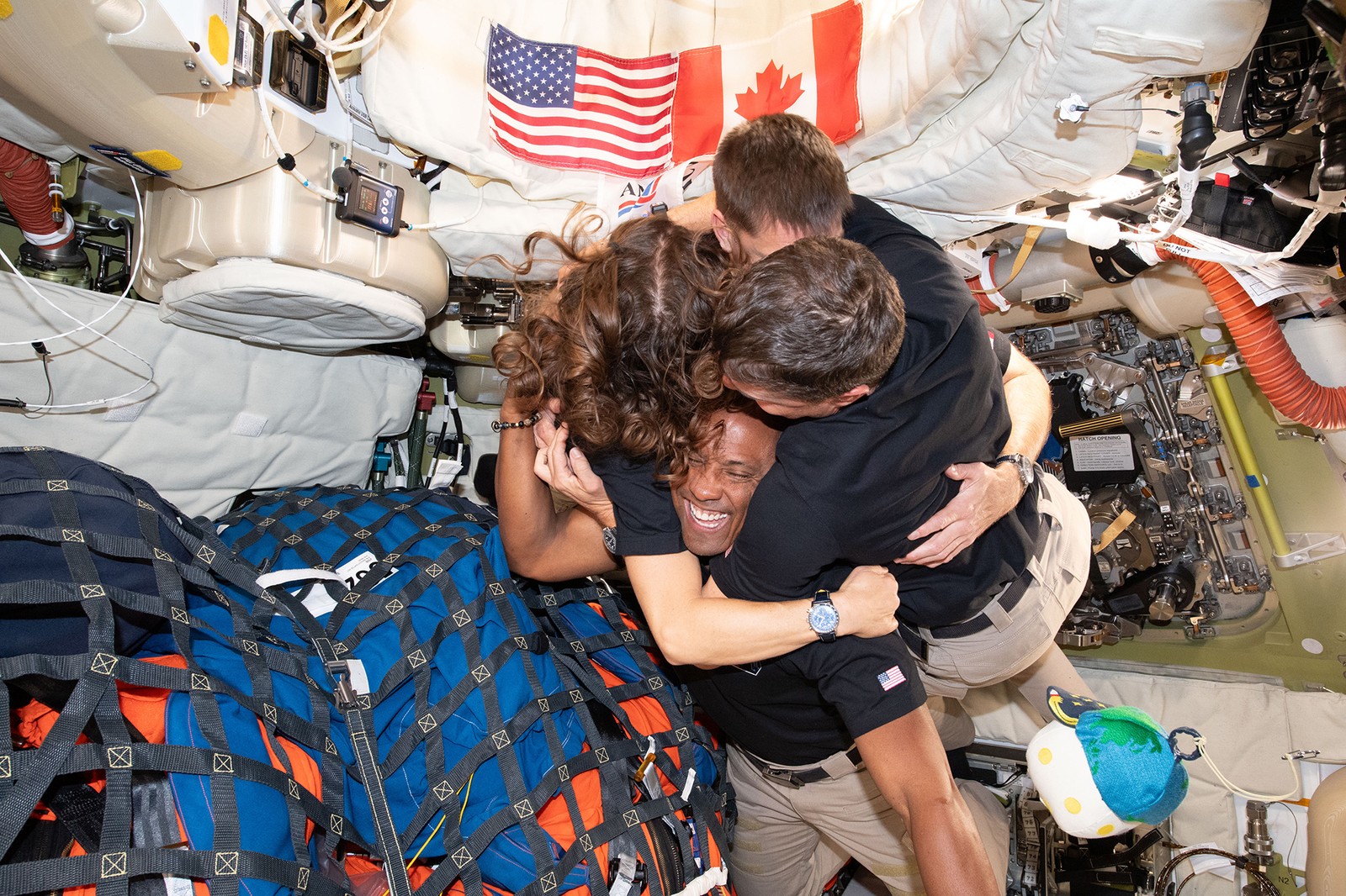Four astronauts hug while inside a capsule, floating in micro-gravity.