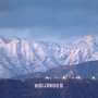 A distant view of the famous "Hollywood" sign, with snow-covered mountains in the background.
