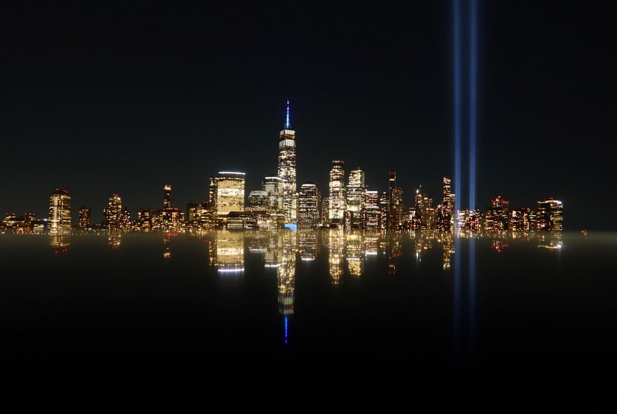 A night view of the New York City skyline, with two shafts of light reaching skyward