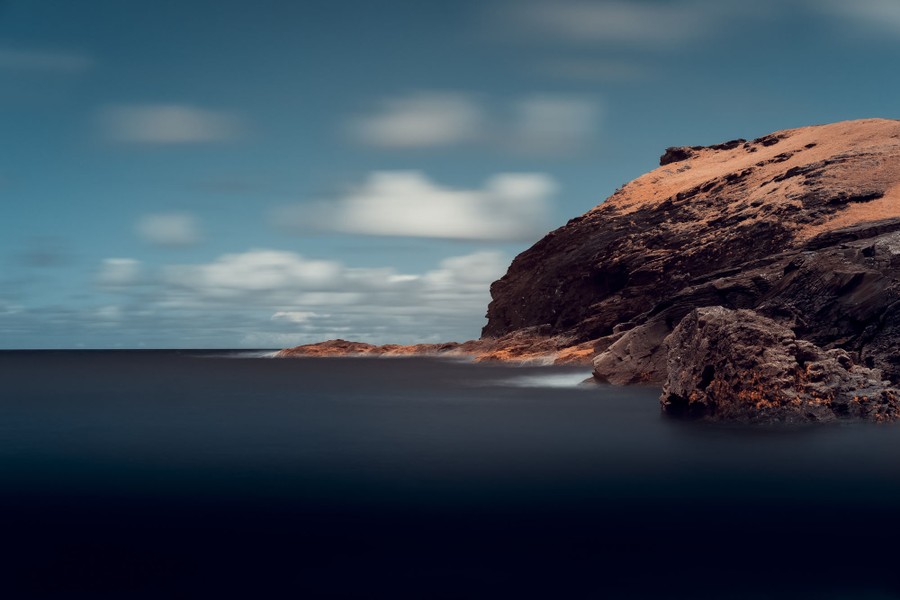 A long exposure image of a rocky coastline and a partly cloudy sky