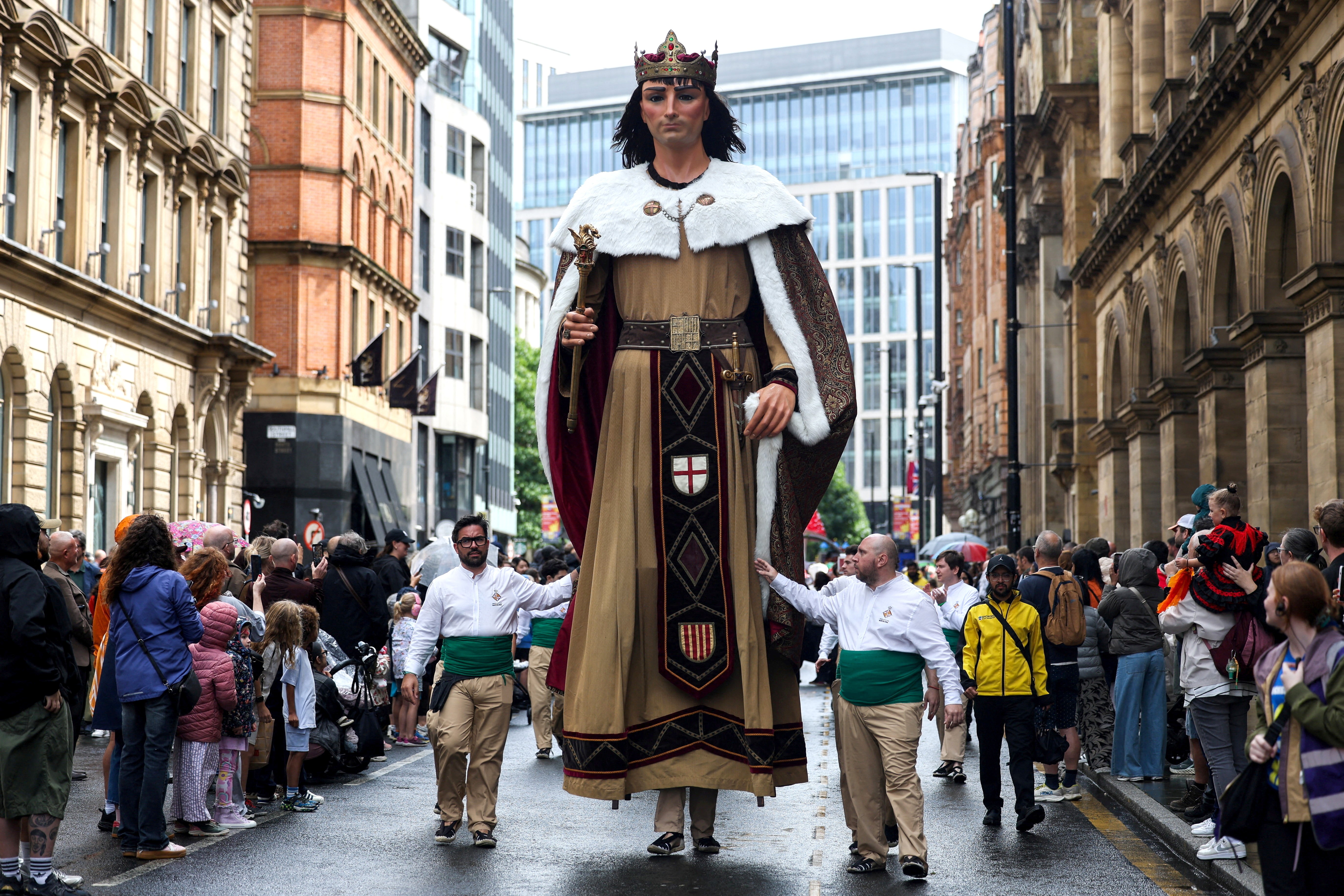 A very tall puppet walks a parade route, escorted by two guides.