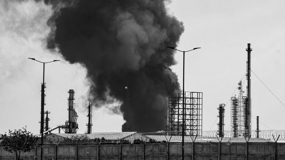 Black-and-white photograph of smoke rising over an oil refinery in Tehran
