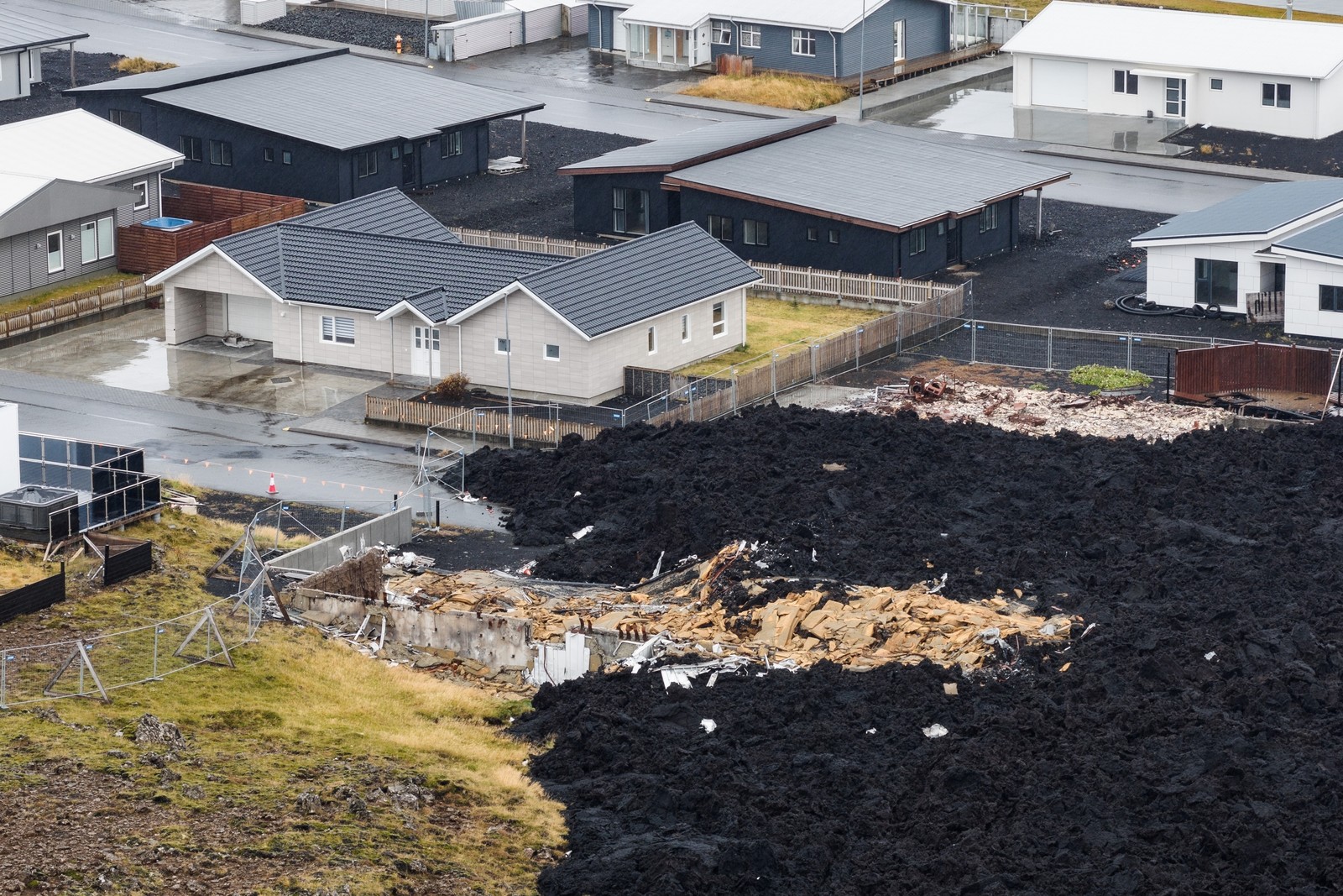 Houses in a neighborhood, seen beside the front edge of an older lava flow that has cooled and hardened atop the ruins of at least one house.