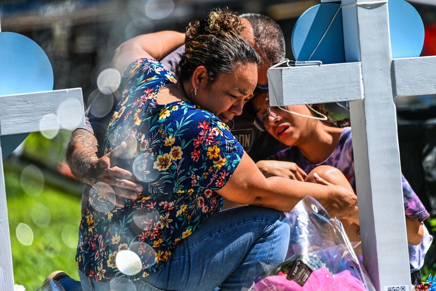 Several people hold one another as they kneel at a makeshift memorial.