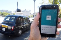 A person holds a phone with the Uber app in front of a black cab.