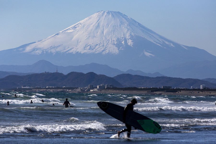 Several people play in the surf, with Mount Fuji in the background.