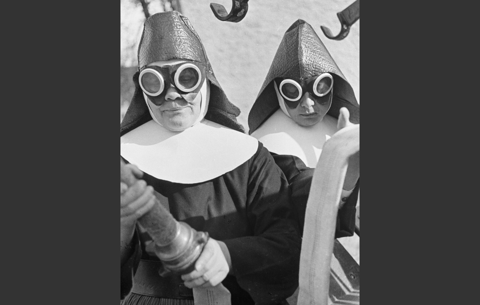 Two nuns wear goggles and hold a water hose.
