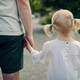 A little girl with pigtails holds an adult's hand.