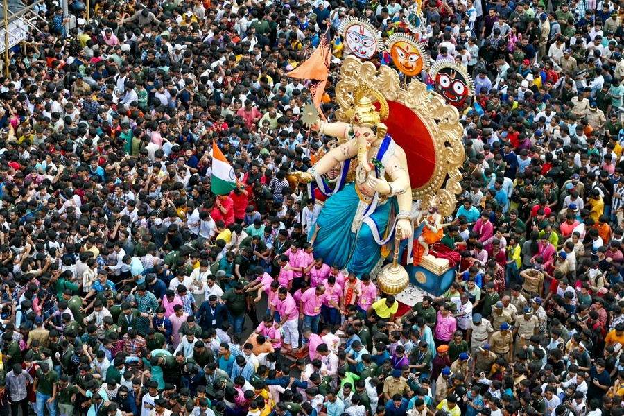 A huge crowd walks around near a large statue of the Hindu deity Ganesha.