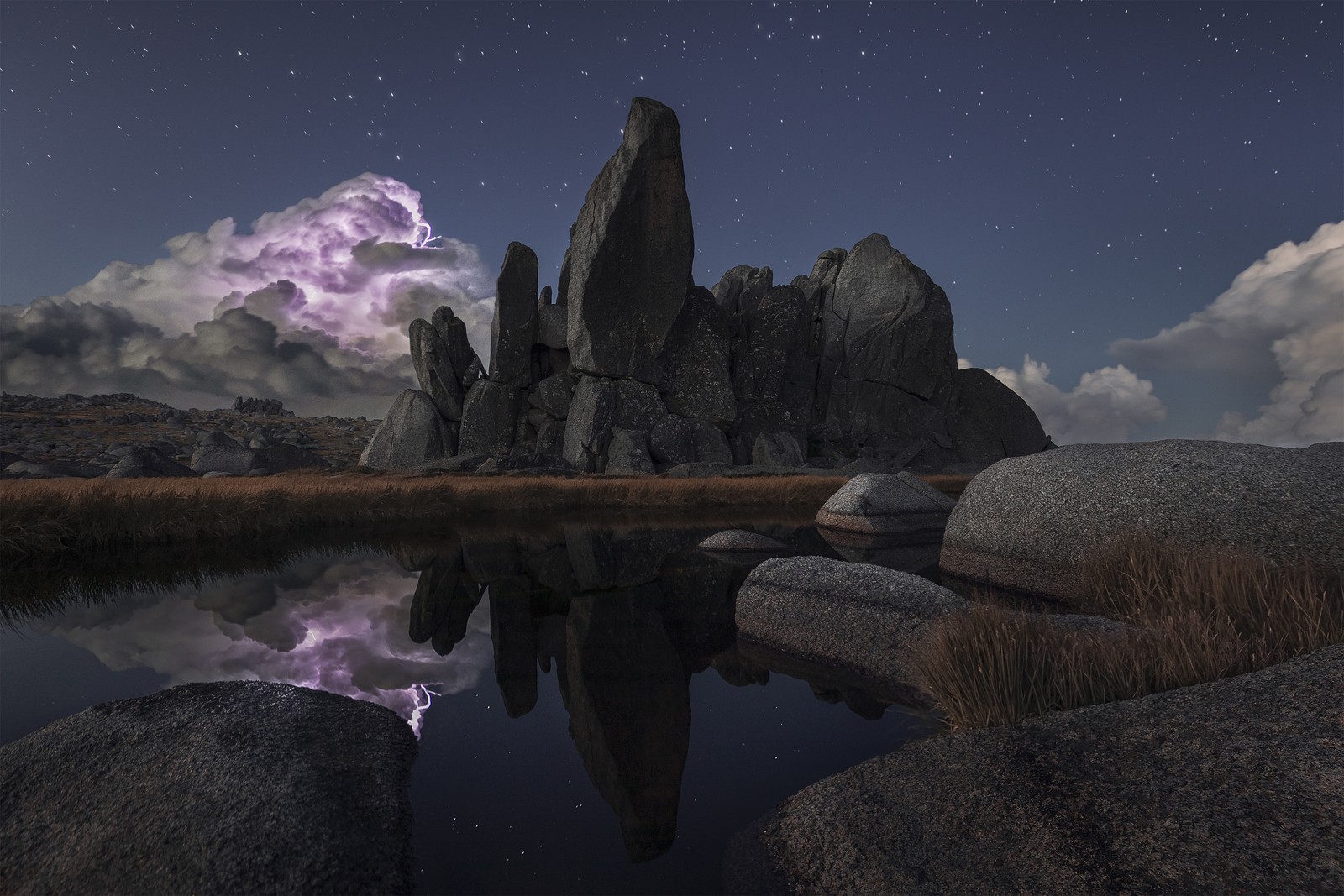 Lightning illuminates a storm cloud behind a large rock formation.