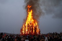 A crowd gathers around a burning temporary wooden structure during a festival.