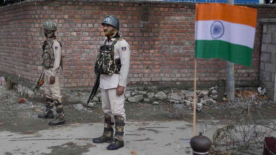 Indian paramilitary soldiers stand guard next to an Indian flag.