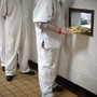 Inmates line up to receive lunch trays through a hole in a cafeteria wall.