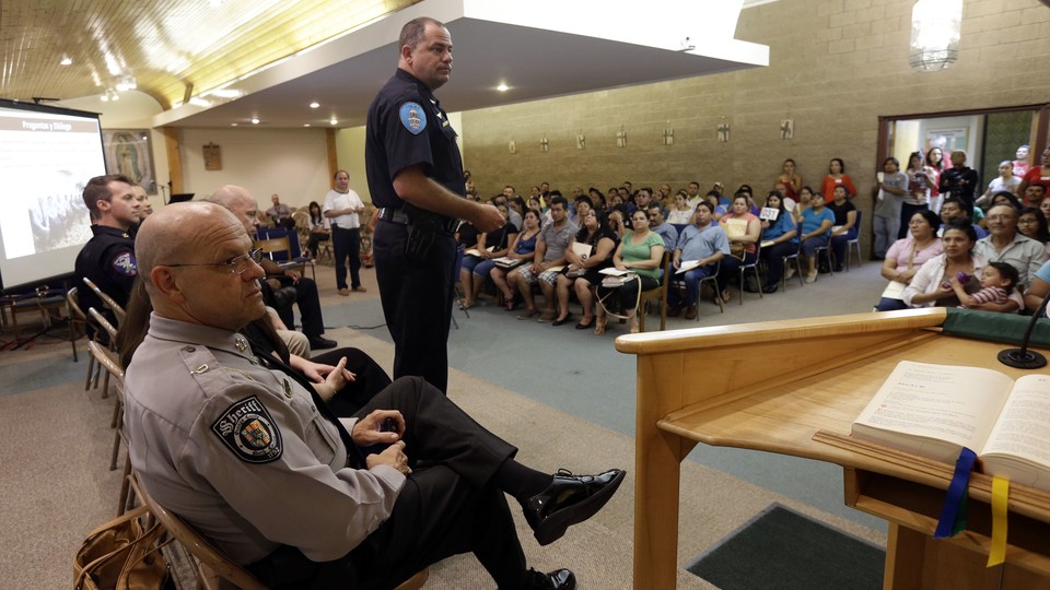 Police officers face rows of Latino residents in a meeting room.