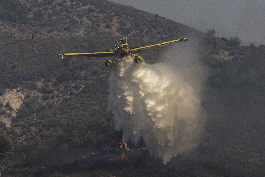 A small aircraft drops water onto a wildfire.