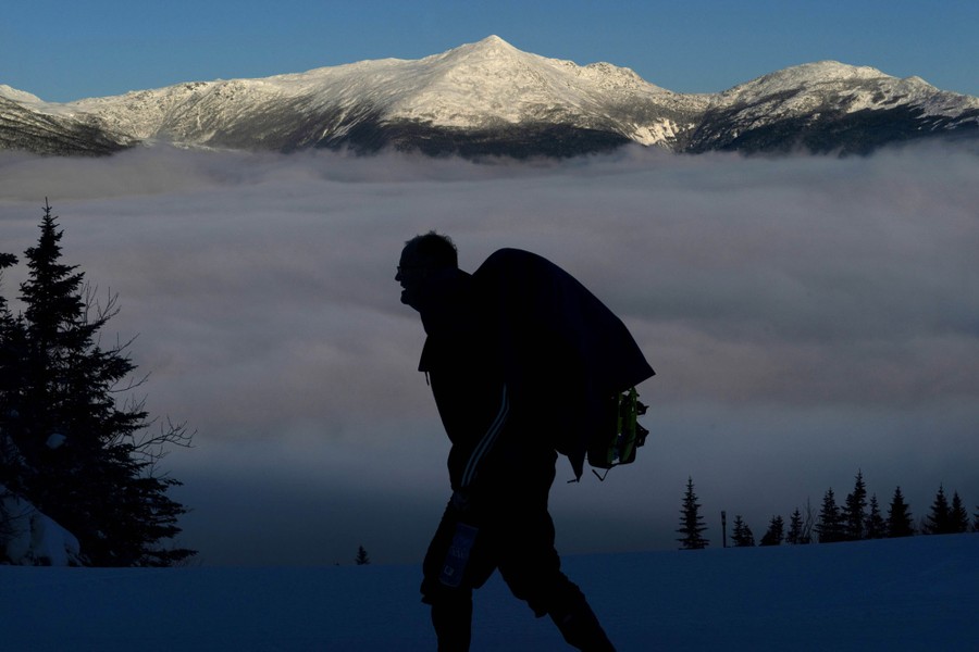 A person carries a backpack, hiking in the mountains near a cloud-filled valley.
