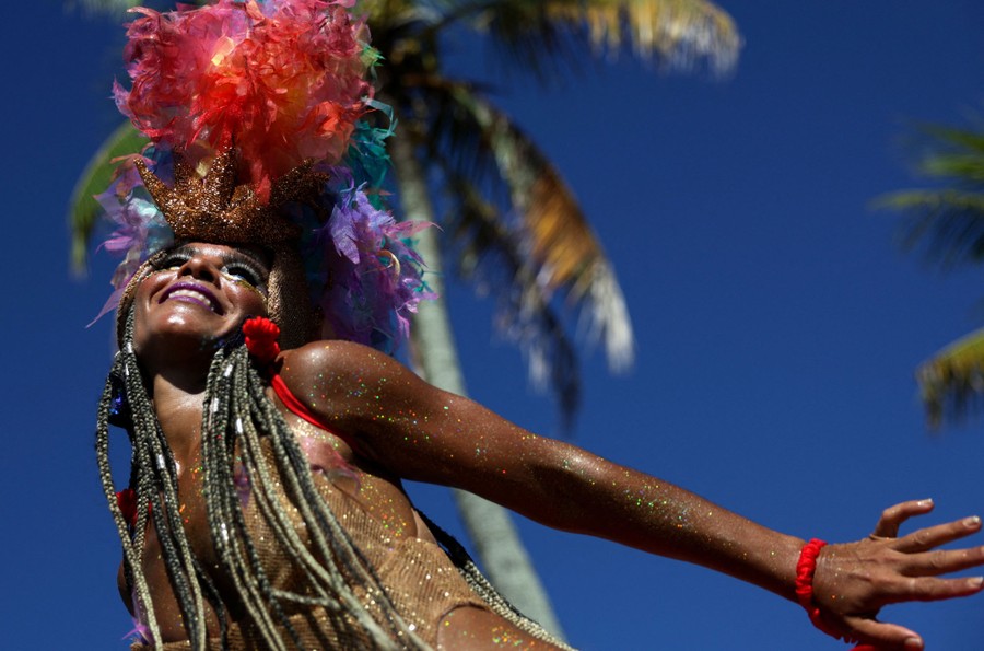 A person in costume and covered in glitter dances under a blue sky.