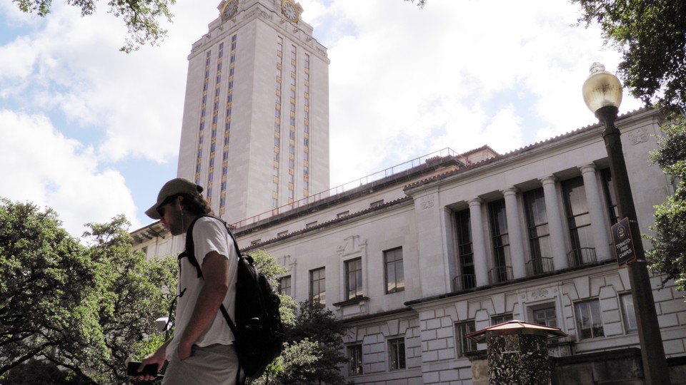 A student walks in front of a clock tower at UT Austin