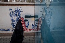 Photograph of a woman wearing a black body covering walking past graffiti of a defaced Statue of Liberty