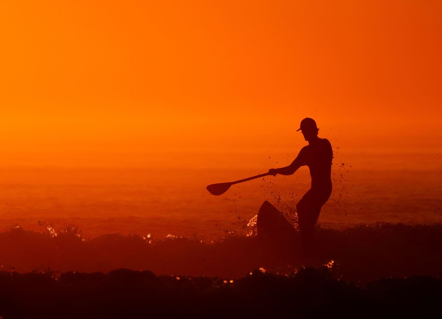 A man on a paddleboard surfs at sunset.