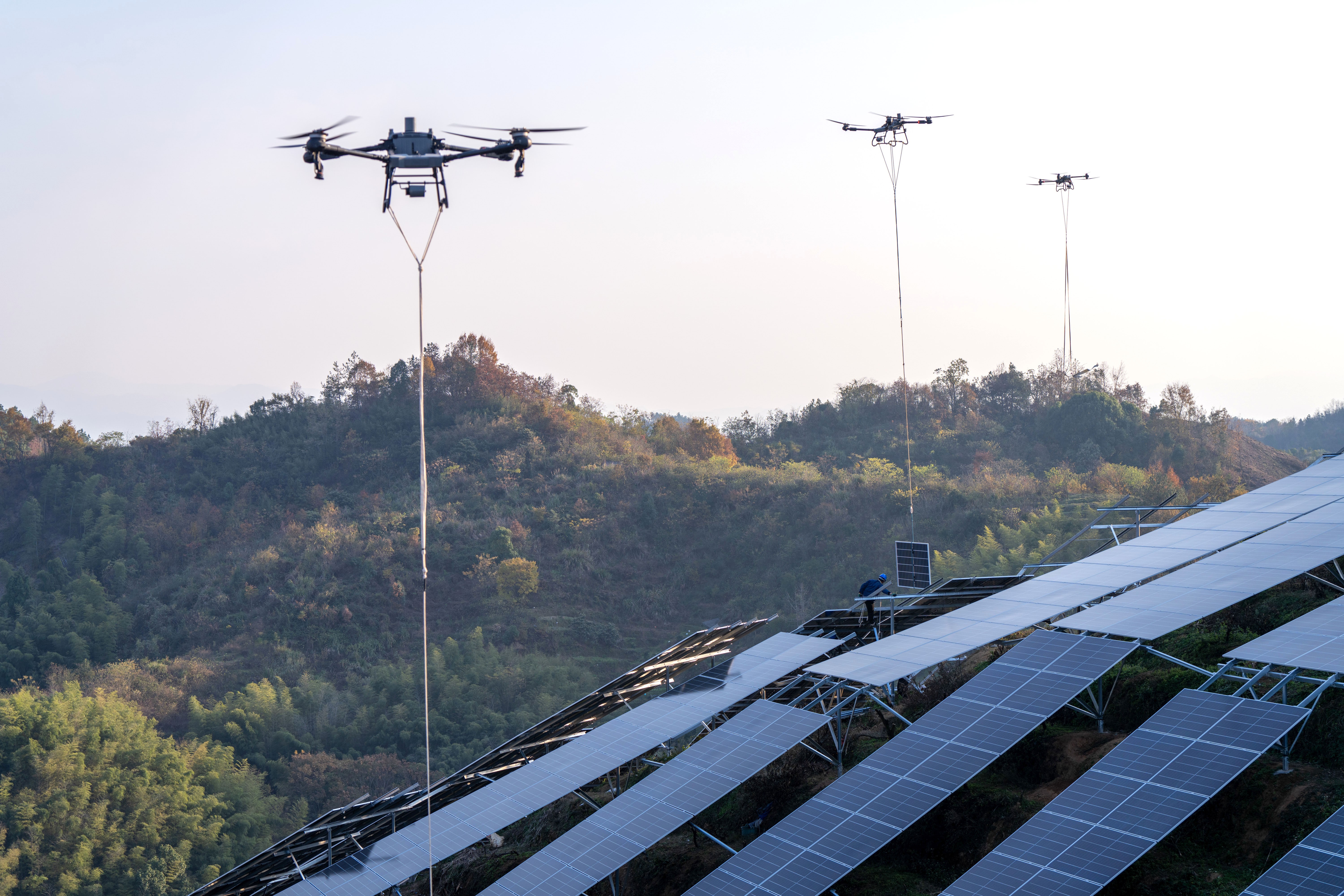 Several drones are used to lift and place solar panels along steep hillsides.