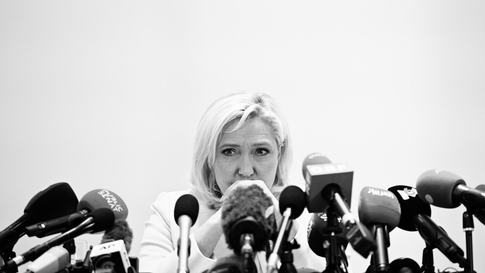 Marine Le Pen sits behind a row of press microphones.