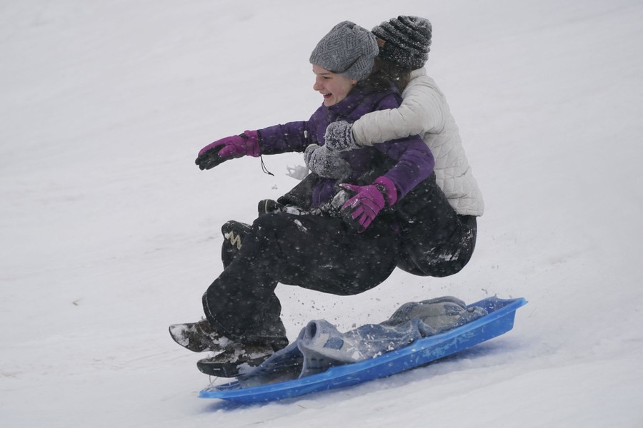 Two young people bounce above their sled as they slide downhill.