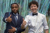 Two young men giving the thumbs-up while walking through stringed curtain